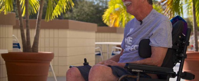 Smiling man in wheel chair relaxes on a sunny patio.