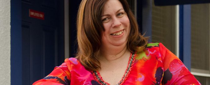 Smiling woman in red top poses in front of women's shelter.