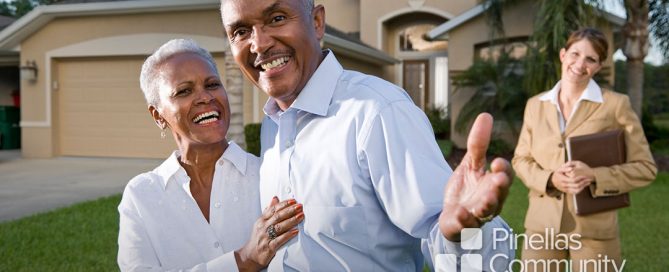 Older adult, happy couple in front of new home with their realtor.