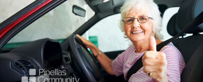 Elderly woman sitting behind the wheel of a car giving a thumbs-up.