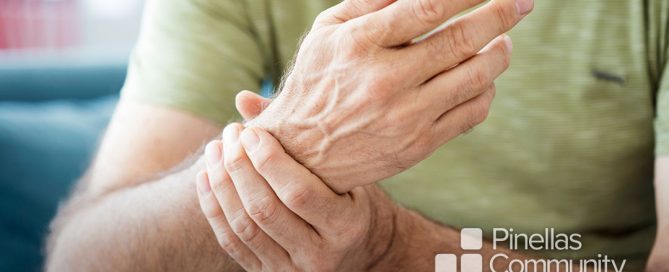 Elderly man rubs aching wrist while discussing pain management options with doctor.