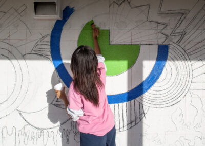A young female volunteer paints a mural on the wall.