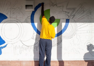 Young male volunteer paints a mural on the wall.