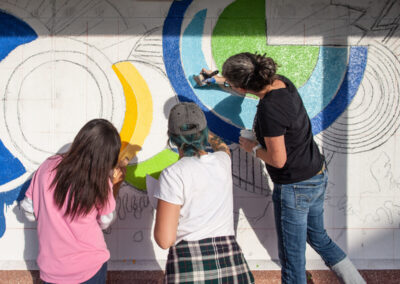 Carrie Boucher and volunteers paint a mural on the wall.